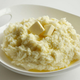 Mashed potatoes topped with butter in a white dish on a white background